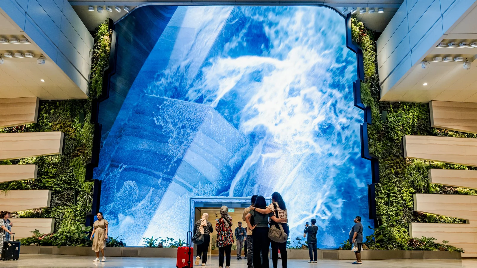 The Wonderfall at Singapore Changi Airport Terminal 2 — a four-storey curved LED waterfall set inside vertical gardens, with travellers gathered at its base for scale